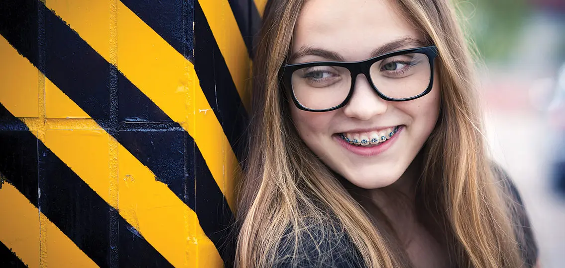 Portrait of smiling teenage girl with braces standing by the black and yellow striped warning wall