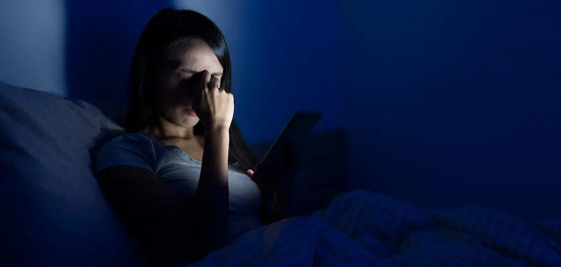 tired Woman feeling headache bed with mobile phone at night feeling mom guilt