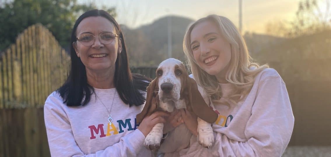 Author Mollie Davies and her mom with a basset hound wearing matching sweaters and smiling outdoors