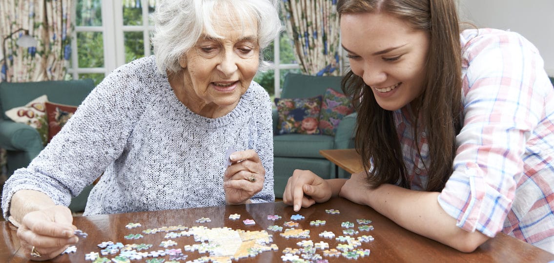 Teenage Granddaughter spending family time with Grandmother With Jigsaw Puzzle