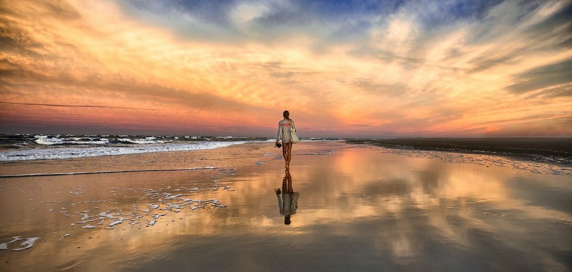 young and beautiful woman walking on the beach near the ocean and walking away at the sunset