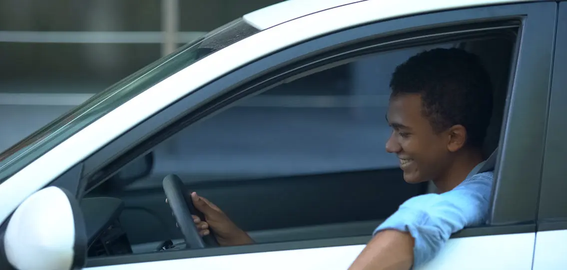 Joyful African-American teen boy sitting on driver place, first car purchase learning to drive