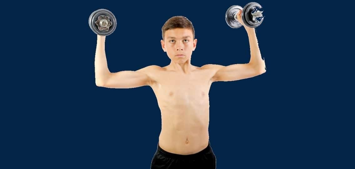Skinny teenage boy athlete lifting weights blue background