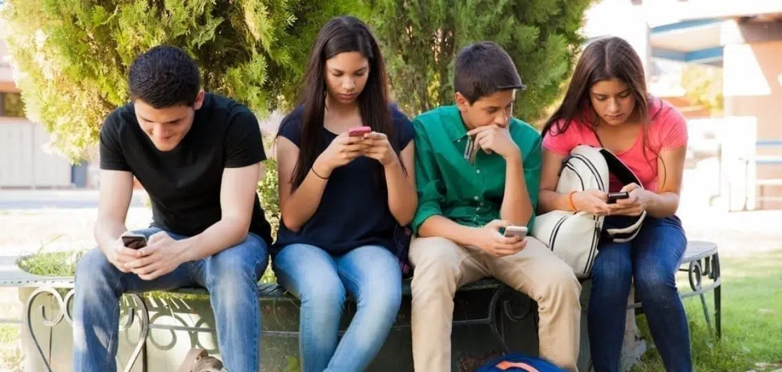 teens hanging out on a bench texting outside