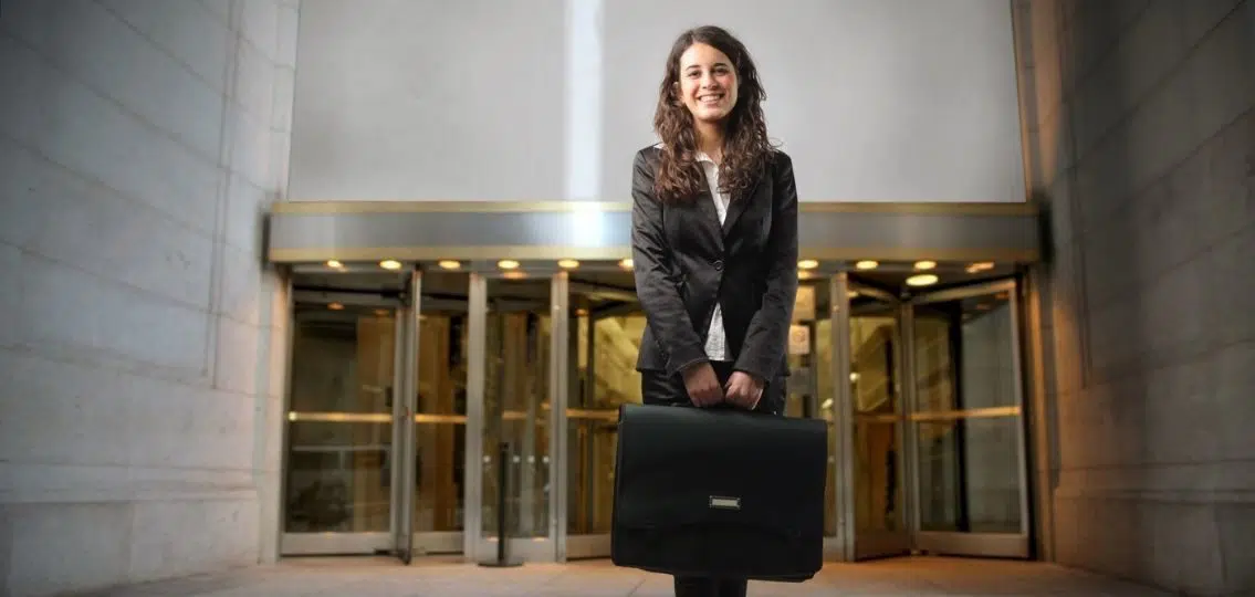 A young woman in a suit with a briefcase in front of an office building getting ready for her first job after graduation