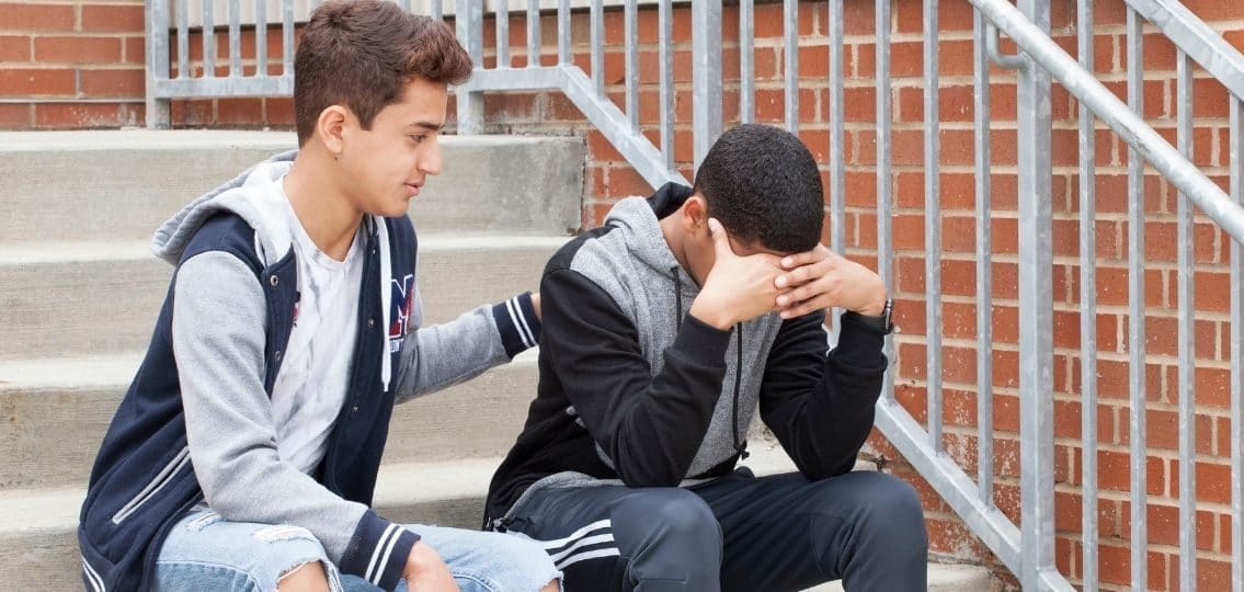 teenager emotional flooding overwhelmed in front of a school being comforted by his friend on the stairs
