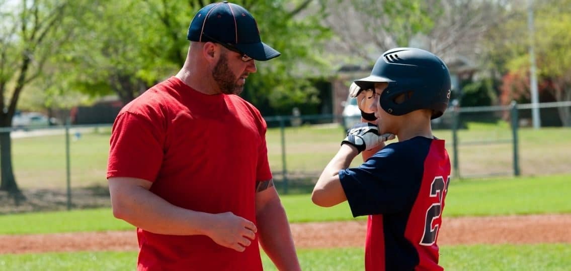 a little league coach talking to a teen player on a baseball field