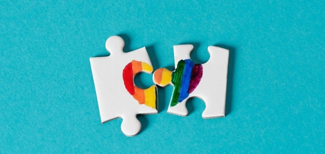 two puzzle pieces with a rainbow heart overlapping on both pieces representing queer teens