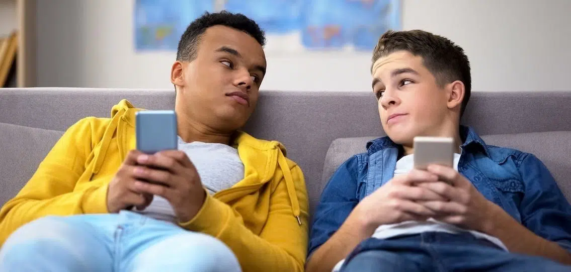 two teen boys wearing hoodies sitting on a couch on their phones exchanging looks wearing what they want to wear