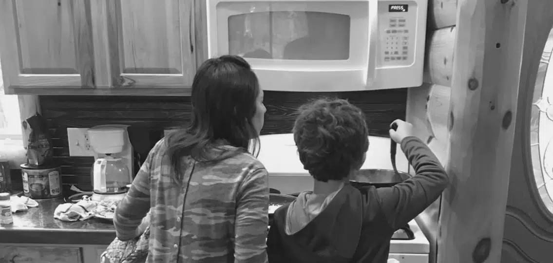 a moody tween boy happily making comfort food on the stove with his mom black and white