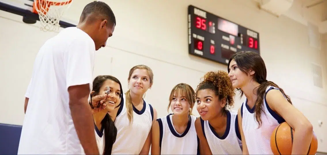 teen girls on a basketball team talking to their coach