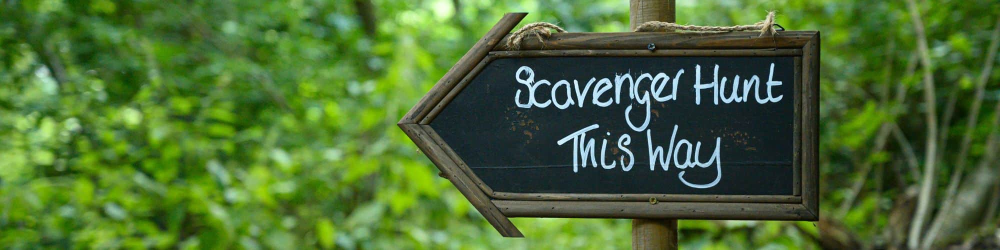 A sign for a scavenger hunt birthday party in the woods reading Scavenger Hunt This Way