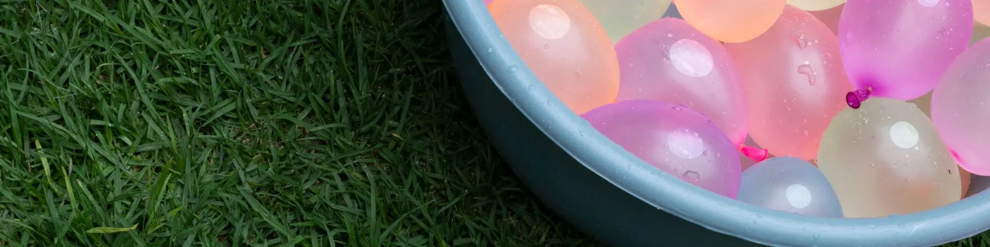 A close up of water balloons in a bin on the grass