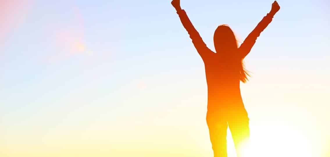 woman in front of a sunrise silhouette worry free cheering