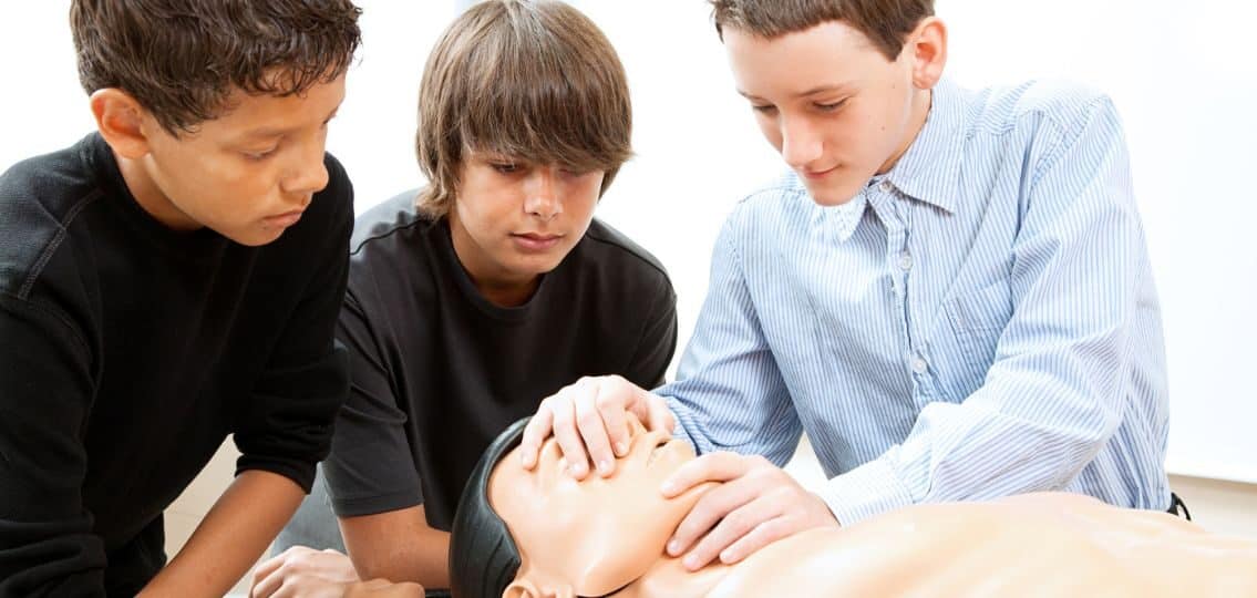teen boys learning safety skills practicing cpr on a cpr dummy