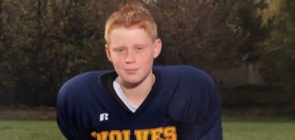 a red headed boy getting a picture taken in his football uniform