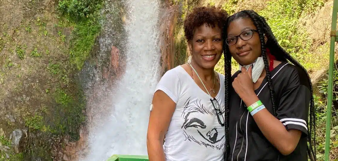 A mom connecting with her teenage daughter on a hike posing in front of a waterfall together