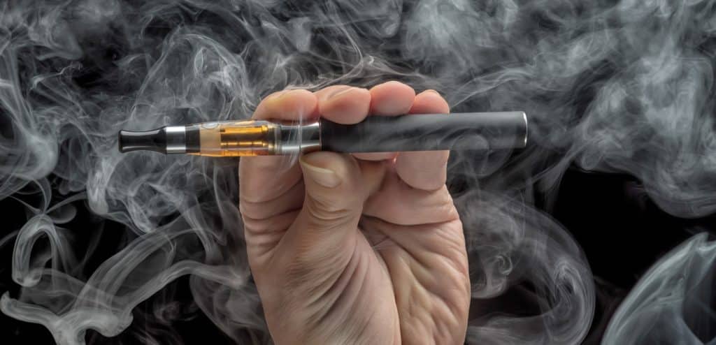 A close up of a teenager vaping, hand holding e-cigarette surrounded by vaping smoke