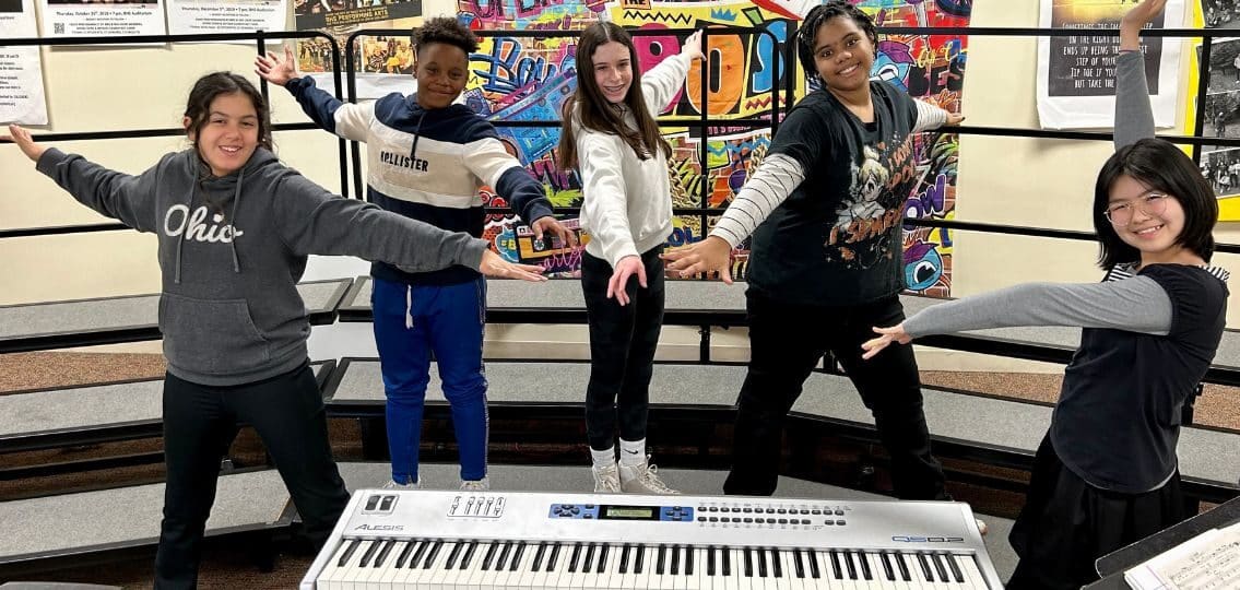 A group of high school teens in music class posing around a keyboard