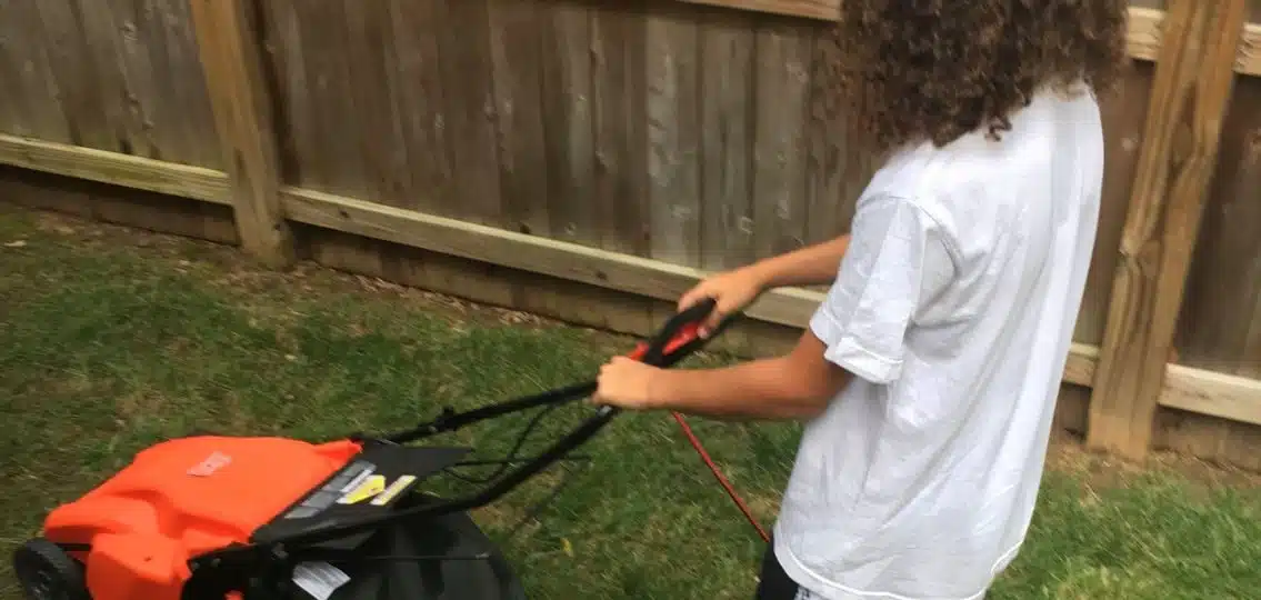 A young teen boy mowing the lawn