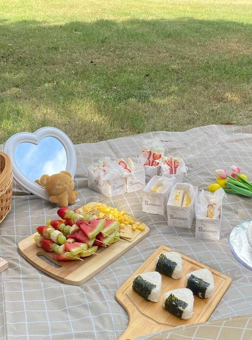 cutting boards with fruit on skewers and onigiri, along with other snacks, on a picnic blanket