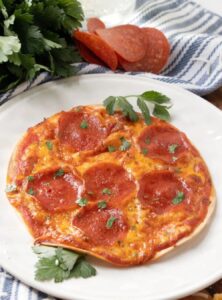 pepperoni tortilla pizza on a plate with a small pile of pepperoni beside the plate