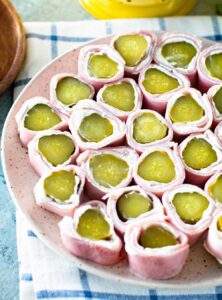 plate of appetizers made by wrapping pickles in cream cheese and deli ham slices