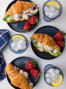 three plates with a chicken salad sandwich and two strawberries each, and three glasses of water with lemon slices