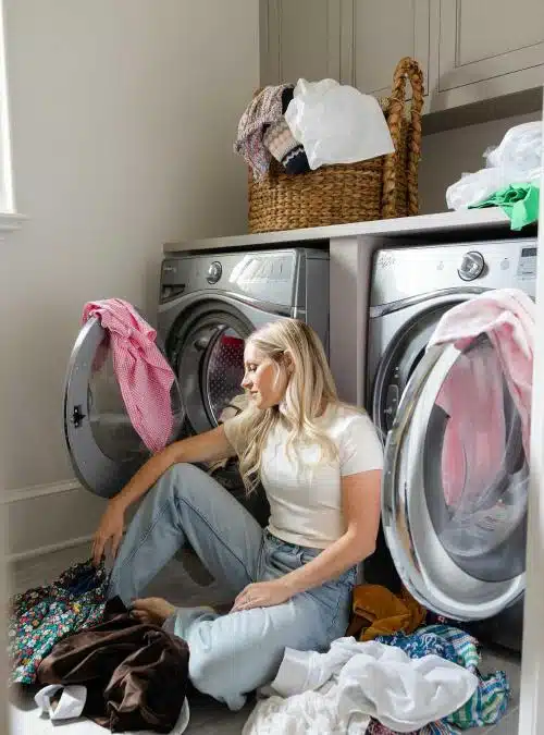 woman sitting in front of a washer and dryer with laundry all around her