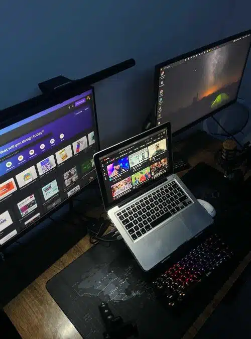 a person wearing headphones sitting in front of a laptop and two large monitors