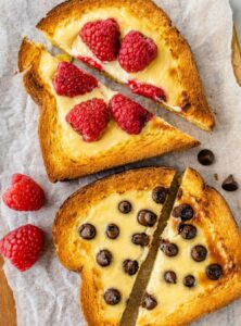 a piece of toast with custard and raspberries and another piece with custard and chocolate chips