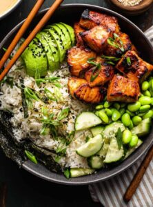 rice, salmon, avocado, sliced cucumbers, and edamame in a bowl