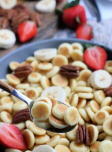 a bowl of mini pancakes with pecans, sliced bananas, and strawberries