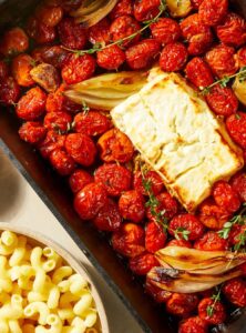 block of feta cheese surrounded by cherry tomatoes in a baking pan