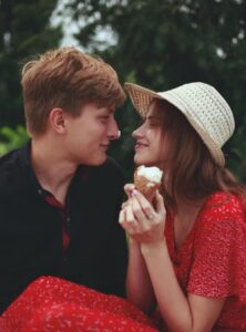Two teens sitting side-by-side, turned to smile at each other. One teen is holding an ice cream cone.