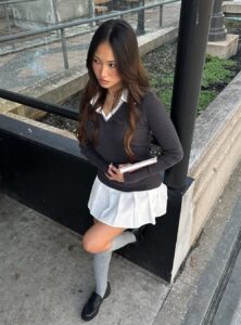 a woman wearing a black long-sleeve ribbed top over a white collared shirt with a short white skirt