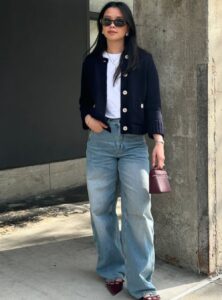 woman with long black hair wearing sunglasses, a white t-shirt, a black sweater, and wide-leg jeans