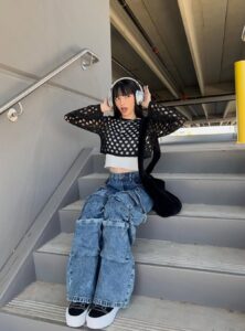 girl sitting on steps wearing a black mesh sweater over a white cropped top with wide-leg cargo jeans