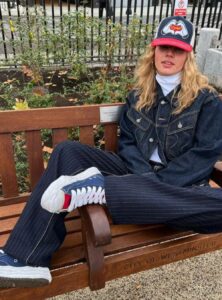 woman wearing a trucker hat, a white turtleneck, an oversize denim jacket, pinstripe pants, and red and blue sneakers