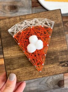 a small square piece of wood with string art in the shape of a slice of pumpkin pie