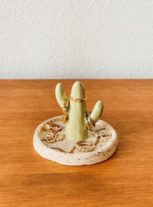 clay jewelry holder in the shape of a cactus with a round base that is holding more jewelry